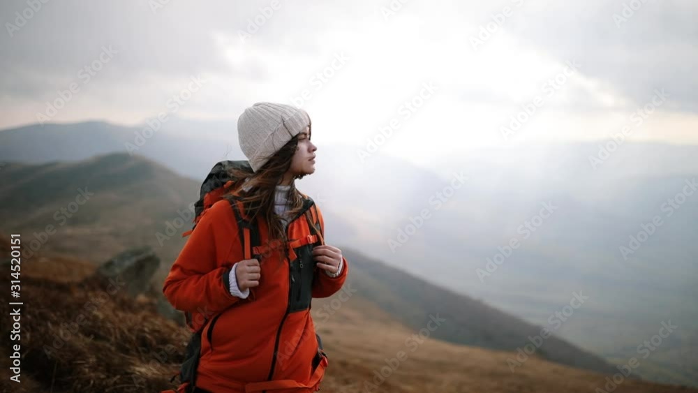 Young beautiful woman tourist stands on top of mountain and enjoys incredible view. Hair blowing in the wind. Girl admiring mountain landscape. Romantic girl enjoys freedom in the mountains Young beautiful woman tourist stands on top of mountain and enjoys incredible view. Hair blowing in the wind. Girl admiring mountain landscape. Romantic girl enjoys freedom in the mountains