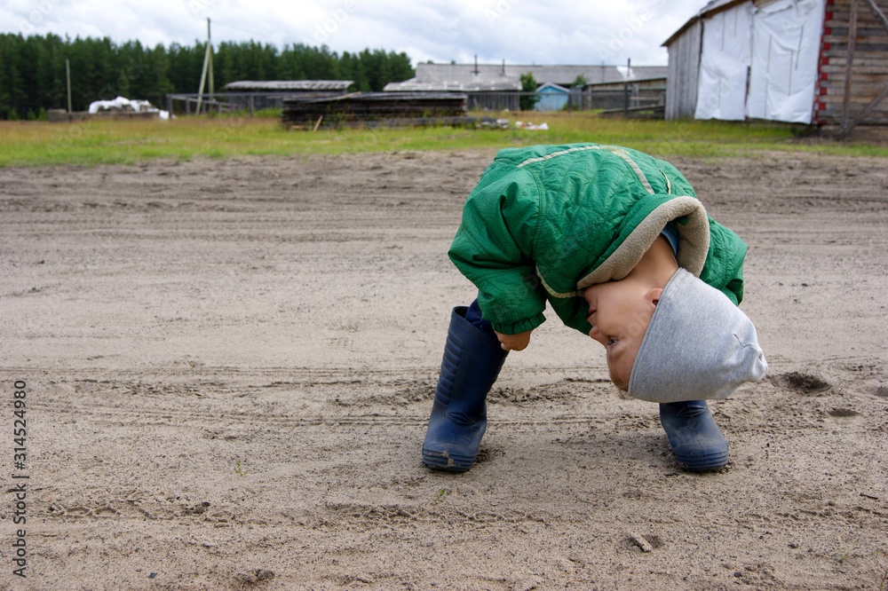 A boy in a green jacket and gray hat and rubber boots leaned over and smiled A boy in a green jacket and gray hat and rubber boots leaned over and smiled
