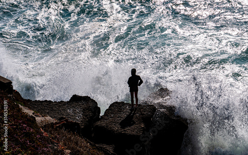 Silhouetted figure standing on the rocks  watching large waves crashing. Taken near praia das ma    s in Portugal.