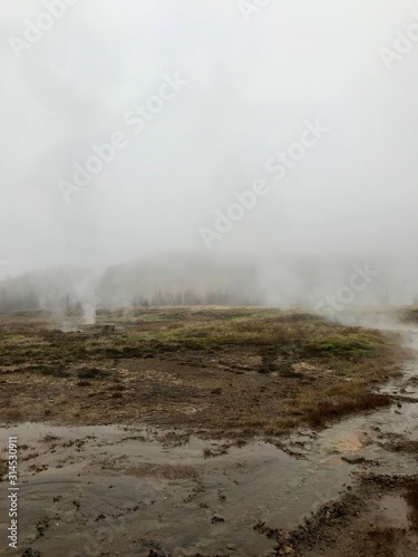Nordic landscape in Haukadalur valley (Iceland) on a cold autumn / winter day in the geothermal area of The Great Geysir: mud roads, rocks & volcanic nature releasing hot water through geyser springs
