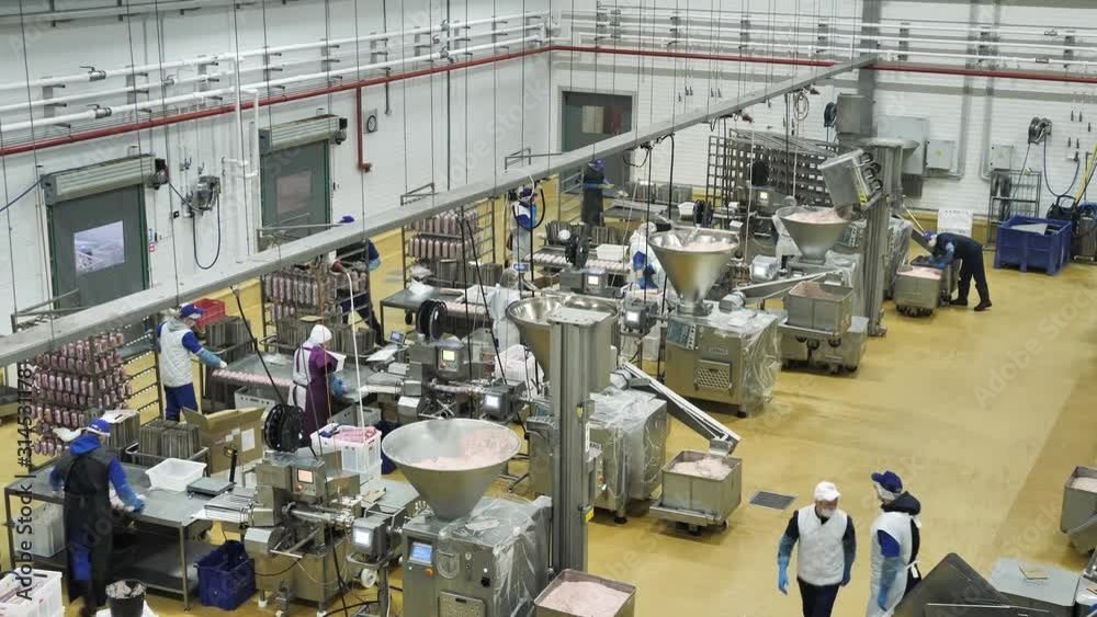 Workers make sausage products on automated production equipment at meat factory