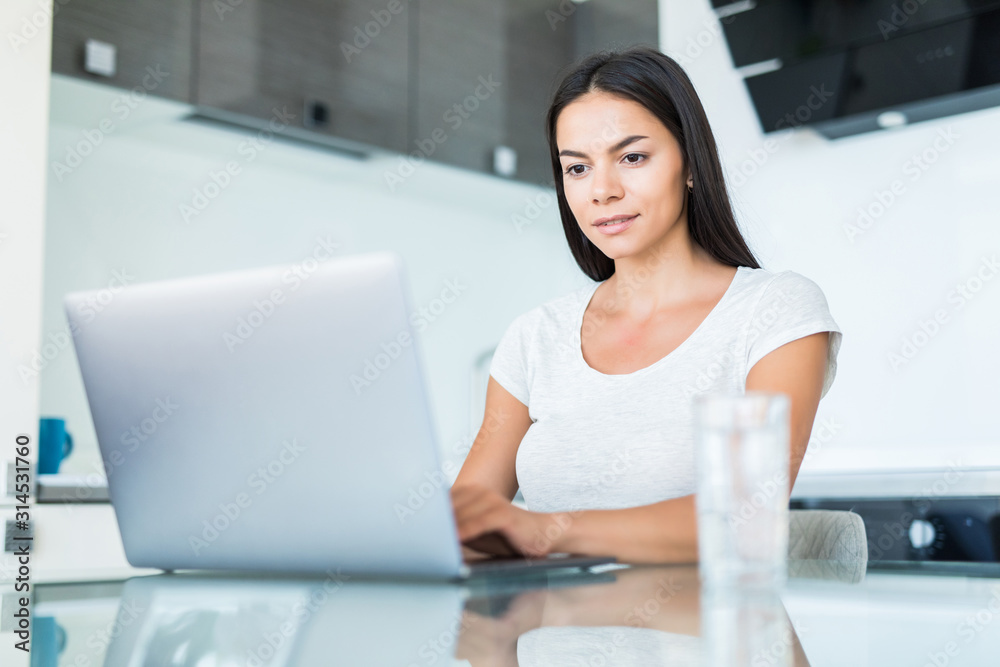 Happy young woman using laptop at counter at home in the kitchen Happy young woman using laptop at counter at home in the kitchen