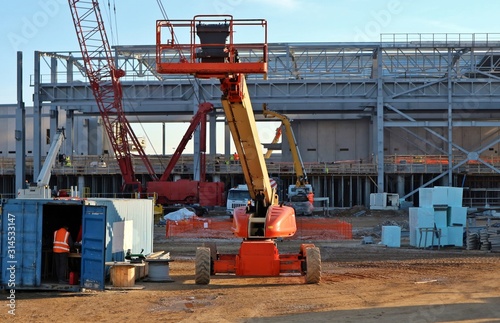 Front view of cherry picker. On background a building under construction  and several machinery and men at work  photo