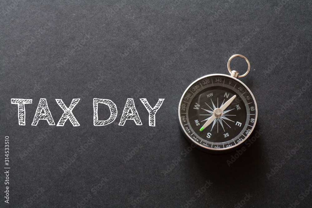 Written TAX DAY words on black background with compass Written TAX DAY words on black background with compass
