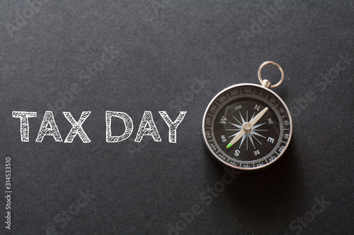 Written TAX DAY words on black background with compass photo