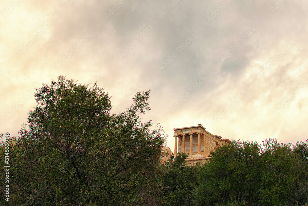 Beautiful landscape photo of Temple of Athena Nike. Dedicated to the goddess Athena Nike. Built around 420 BC. Tree Leaves Border. Natural Frame. Stormy sky and gloomy clouds. Athens Greece Beautiful landscape photo of Temple of Athena Nike. Dedicated to the goddess Athena Nike. Built around 420 BC. Tree Leaves Border. Natural Frame. Stormy sky and gloomy clouds. Athens Greece