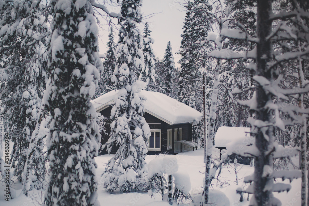 Fototapeta premium A cozy wooden cabin cottage chalet house covered in snow near ski resort in winter with the lights turn on