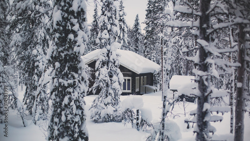 A cozy wooden cabin cottage chalet house covered in snow near ski resort in winter with the lights turn on photo