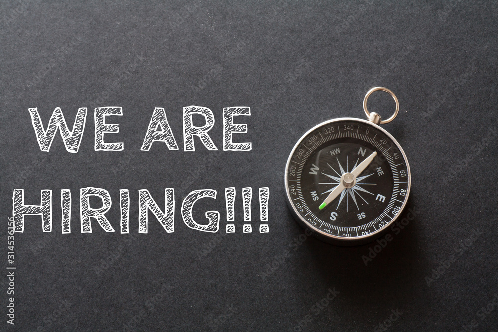 Written WE ARE HIRING words on black background with compass Written WE ARE HIRING words on black background with compass