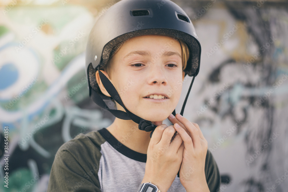 Portrait of trendy young skater at the skatepark wearing helmet, looking away. Smiling teenager enjoying sunny day outdoors in the city with skateboard. Youth, health, safety, sport, positive concept Portrait of trendy young skater at the skatepark wearing helmet, looking away. Smiling teenager enjoying sunny day outdoors in the city with skateboard. Youth, health, safety, sport, positive concept