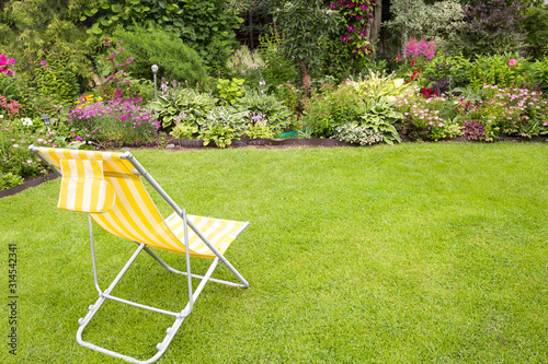 Garden chair on a green grass in a beautiful flower garden in summer