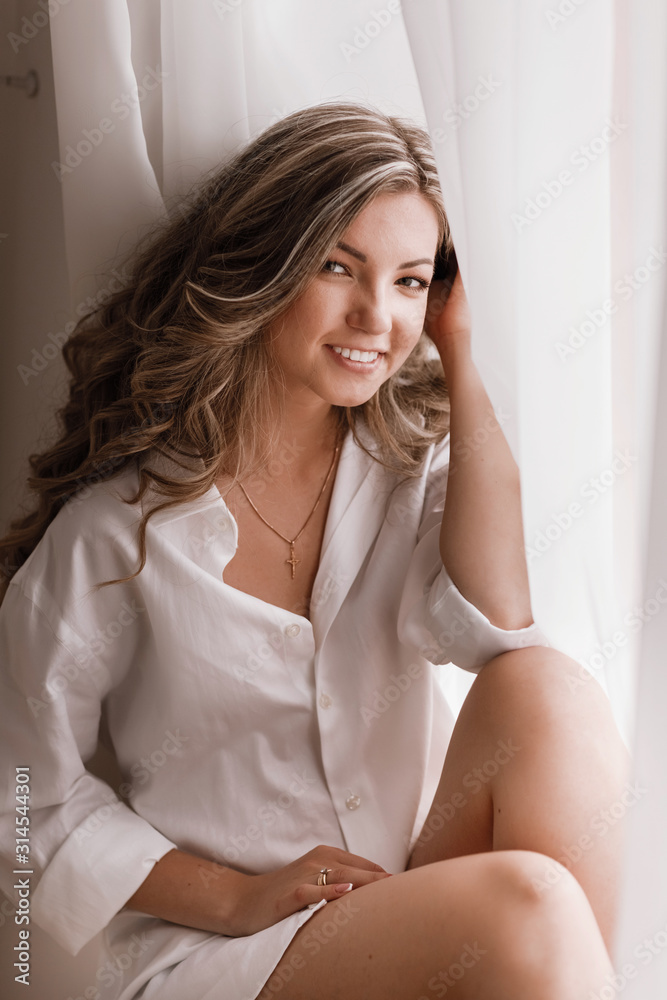 Young female blonde model in window light. Woman near Window. Dream and Relax, tender girl in the Morning in the Bedroom window Young female blonde model in window light. Woman near Window. Dream and Relax, tender girl in the Morning in the Bedroom window