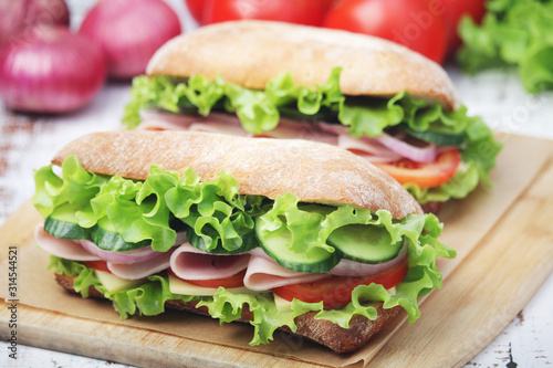 Two sandwiches with fresh vegetables, ham and cheese in ciabatta bread	