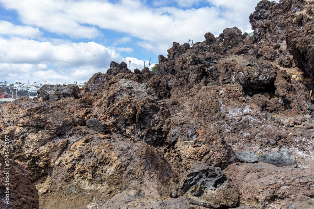 Big lava rocks on the coastline of Puerto del Carmen at Canary island Lanzarote. The sky is blue with white clouds