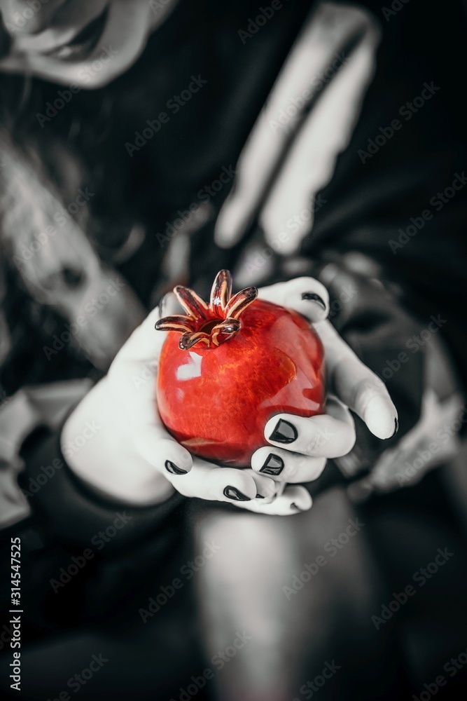 Female hand holding ceramic red pomegranate fruit. Manicure with black nail polish. Black and white photo with red pomegranate - obrazy, fototapety, plakaty 