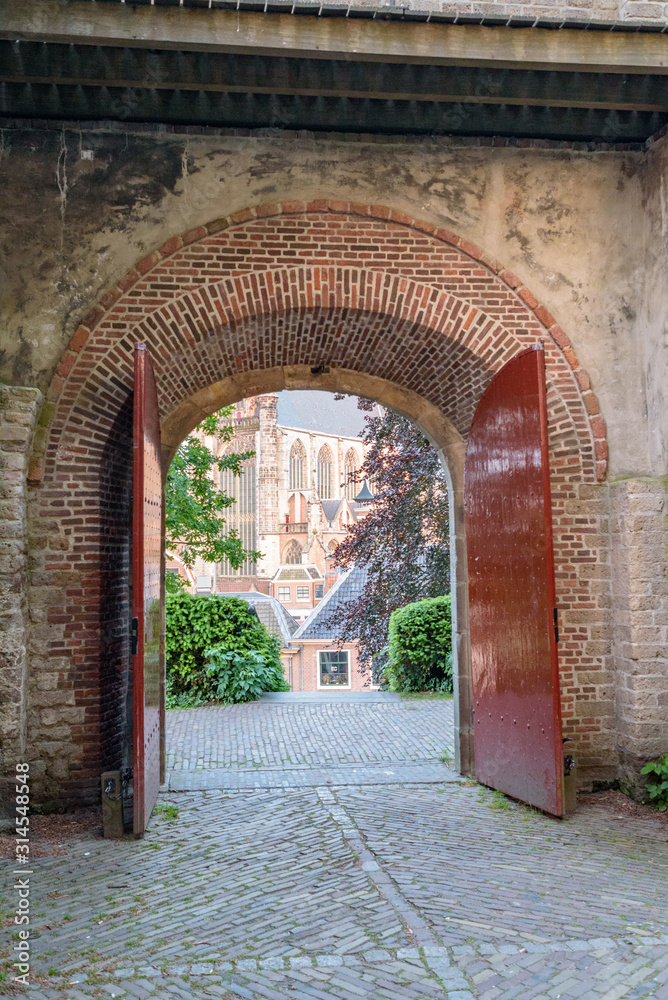 Cathedral in the city of Leiden, The Netherlands, seen through large medieval gate with red doors