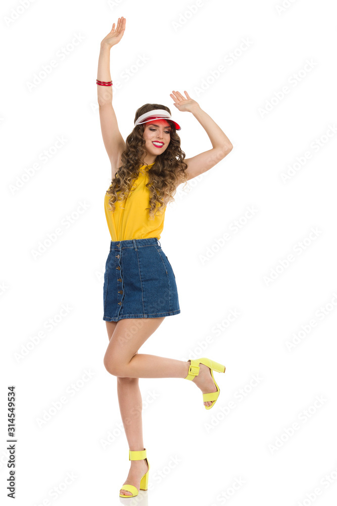 Foto Stock Carefree Young Woman In Jeans Mini Skirt And High Heels Is  Danding On One Leg With Arms Raised | Adobe Stock