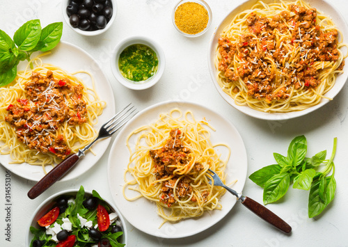 Dining table concept. Spaghetti with Bolognese sauce, vegetable and greens salad with olives, Parmesan cheese and spices