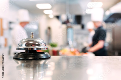 Table distribution in the restaurant. Cooks prepare food in the kitchen against the background of a metal bell.
