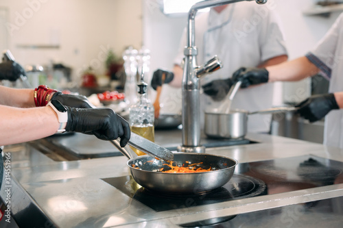 Cooks prepare meals on an electric stove in a professional kitchen in a restaurant or hotel.