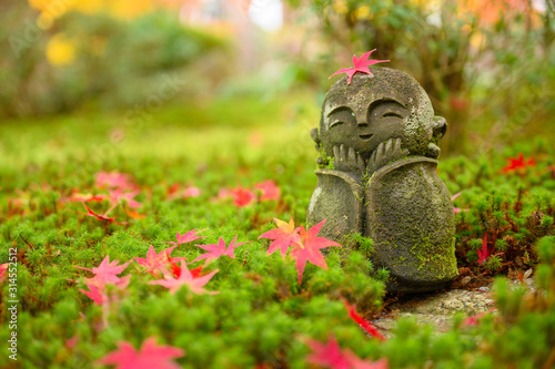 Red Maple leaf on head of Jizo sculpture doll (little Japanese Buddhist monk doll rock) in Japanese Garden.