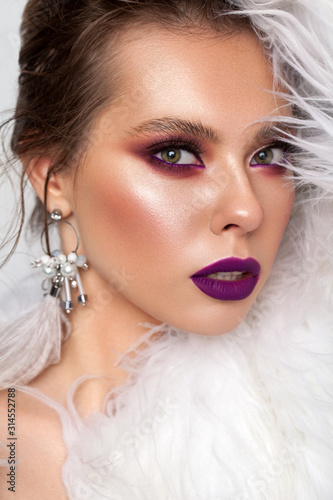 Photo of a very beautiful girl with green eyes, professional purple bright make-up, with earrings from ostrich feathers.