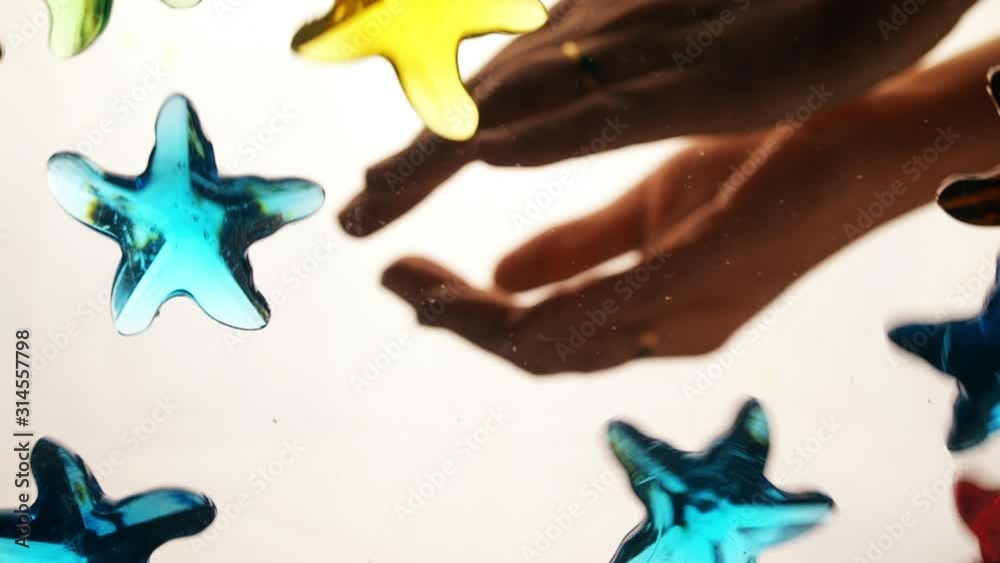 View from below as a hand pours artificial colored starfish. Background for the site, vacation. Indoors. Close up. white background. View from below as a hand pours artificial colored starfish. Background for the site, vacation. Indoors. Close up. white background.