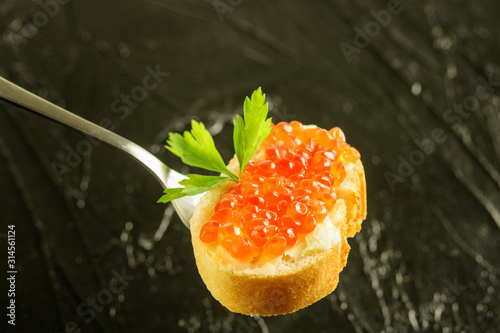 Sandwitch of white fresh bread and red caviar on the fork on the black background.