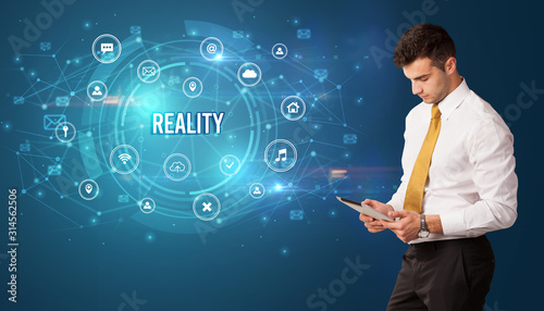 Businessman thinking in front of technology related icons and REALITY inscription, modern technology concept