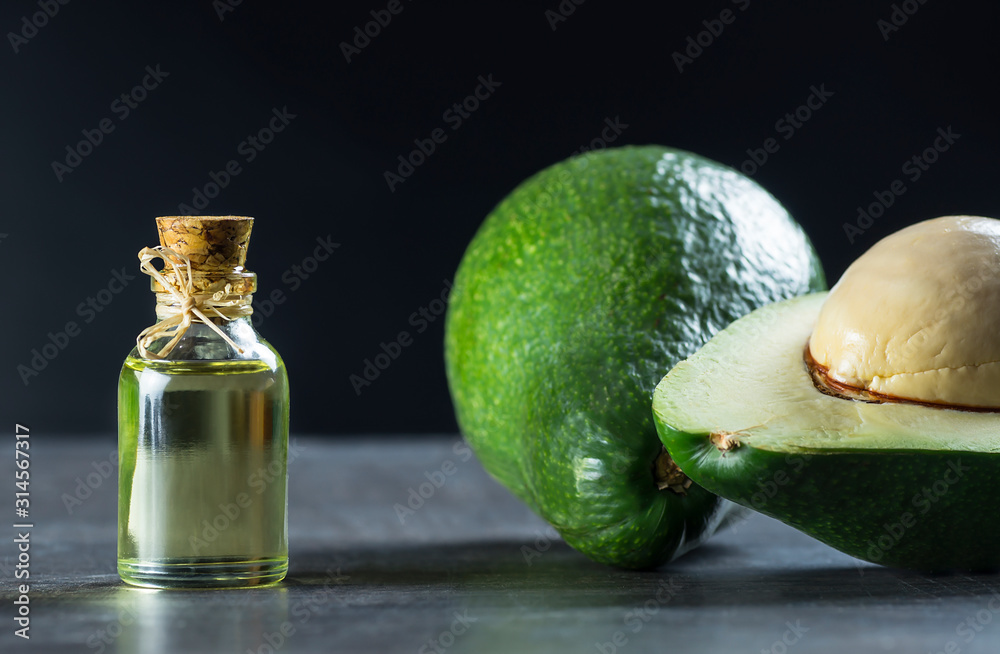 Glass bottle of avocado oil, with fresh avocado fruits on black rustic background, Persea americana Glass bottle of avocado oil, with fresh avocado fruits on black rustic background, Persea americana