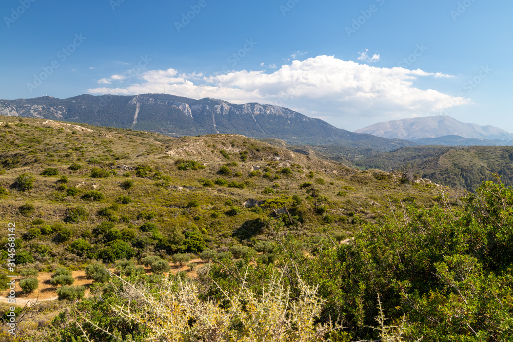 View at landscape on the westside of Greek island Rhodes with green vegetation in the foreground and mountain range in the background