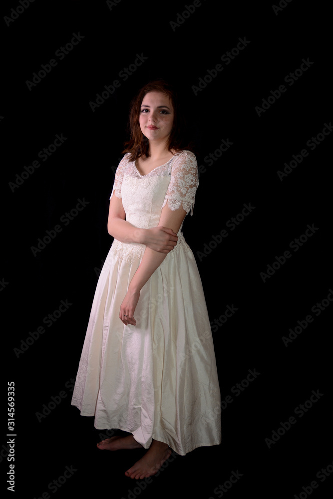 Young woman in white wedding dress stands barefoot against black background Young woman in white wedding dress stands barefoot against black background
