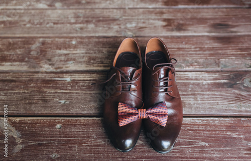 Close-up of leather brown shoes with a bow-tie on a wooden background. Gentleman's, men's set. Business. Wedding shoes, details.