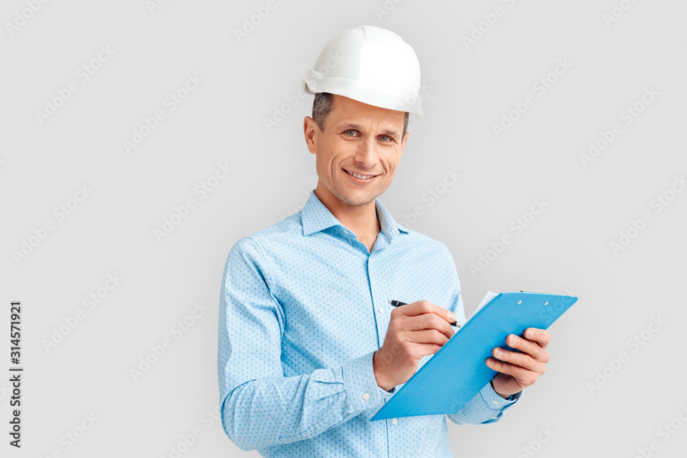 Construction. Mature man in hardhat standing isolated on white with clipboard taking notes smiling joyful Construction. Mature man in hardhat standing isolated on white with clipboard taking notes smiling joyful