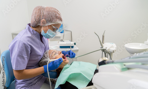 A dentist uses ultrasound and a saliva ejector to clean a patient’s dental calculus.