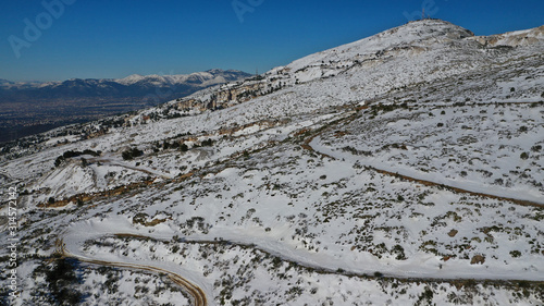 Aerial drone photo of curvy icy road in famous mountain of Penteli covered in white snow during winter time, Attica, Greece
