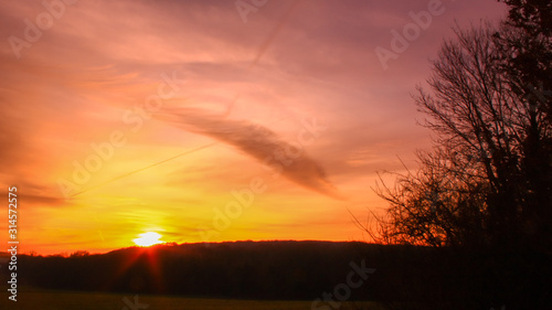 Beautiful multicolored sunset. Cumulonimbus and very colorful stratus in a dramatic sky. Sun disappearing behind a hill.