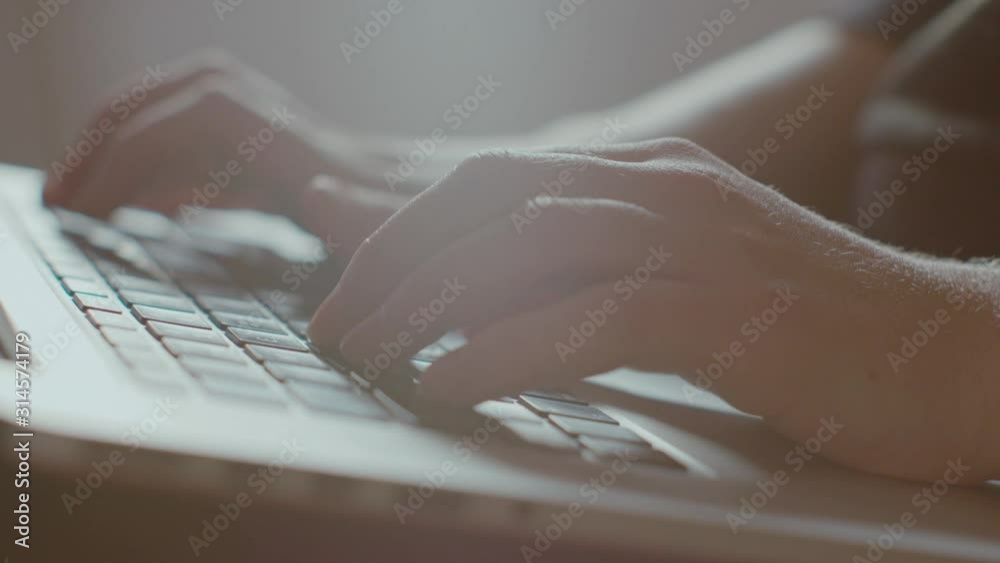 Close up of young female hands typing away writes on a laptop computer keyboard in slowmotion and backlit from a window. Lens flares. UHD.