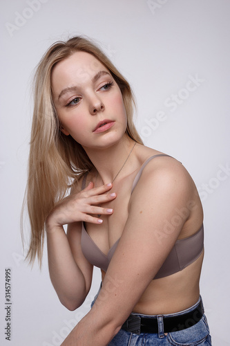 beauty portrait of sexy caucasian woman with long blond hair posing in beige lingerie and blue jeans on white studio background. model tests of pretty girl in bra. attractive female with clean skin