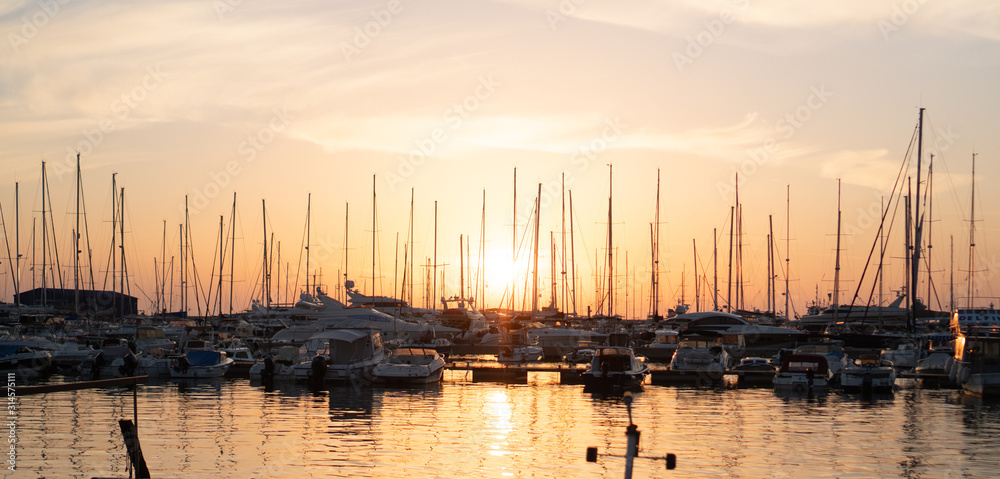Yachts and boats moored to the pier and lit by the setting sun.