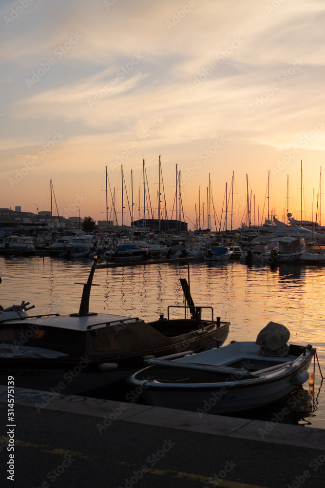 Yachts and boats moored to the pier and lit by the setting sun.