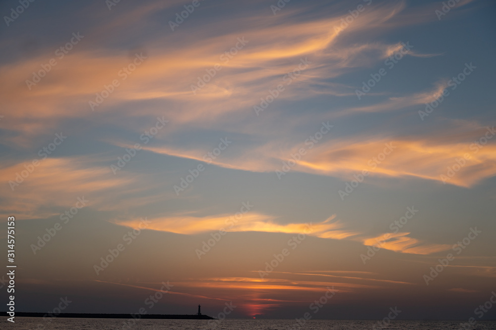 Silhouette of a lighthouse on the horizon in the rays of the setting sun. Colorfull sky
