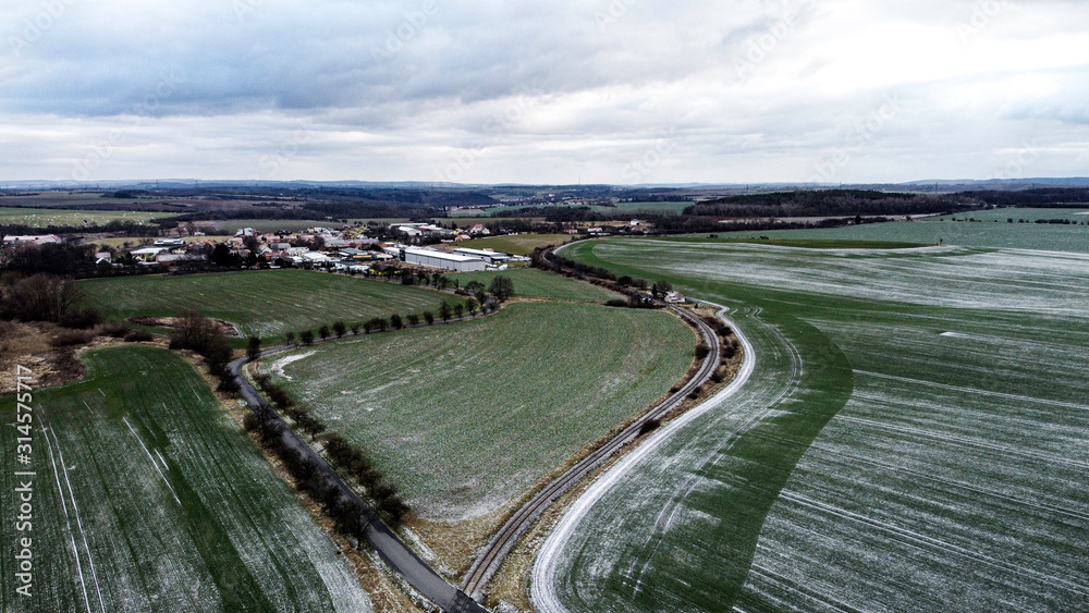 Aerial view of road and railing meandering between fields. In the background you can see a small village. Winter landscape.