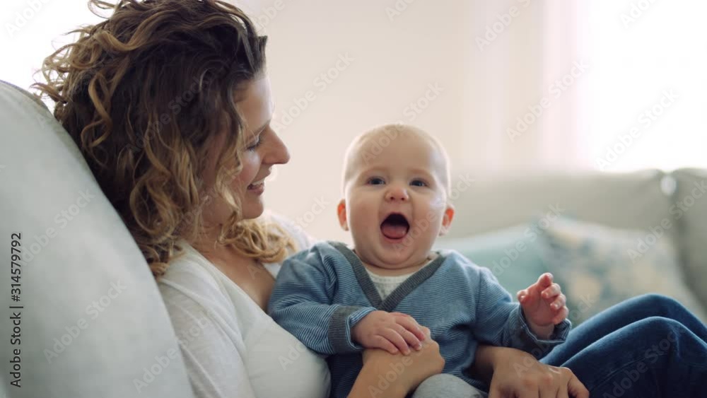 Happy baby looks toward camera and smiles wide as mother lovingly holds him Happy baby looks toward camera and smiles wide as mother lovingly holds him