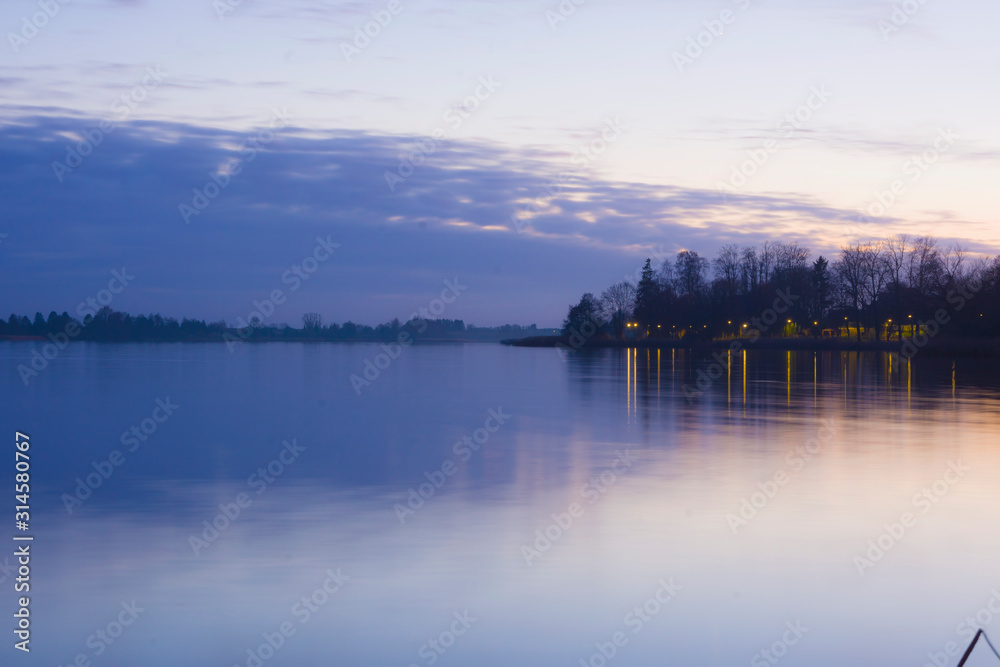 Landscape sunset lake violet sky clouds oranges sun trees on the shore reflection in the water