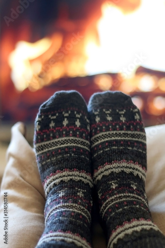 Feet in woolen patterned socks resting by the fireplace. Selective focus.
