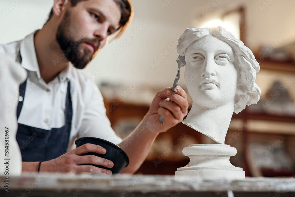 Skillful sculptor makes professional restauration of gypsum sculpture of woman's head at the creative workshop.