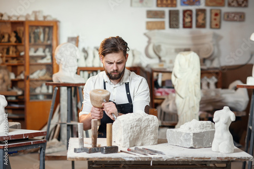 Εκτύπωση καμβά Male sculptor in white shirt and black apron makes a limestone copy of woman torso at the artistic studio