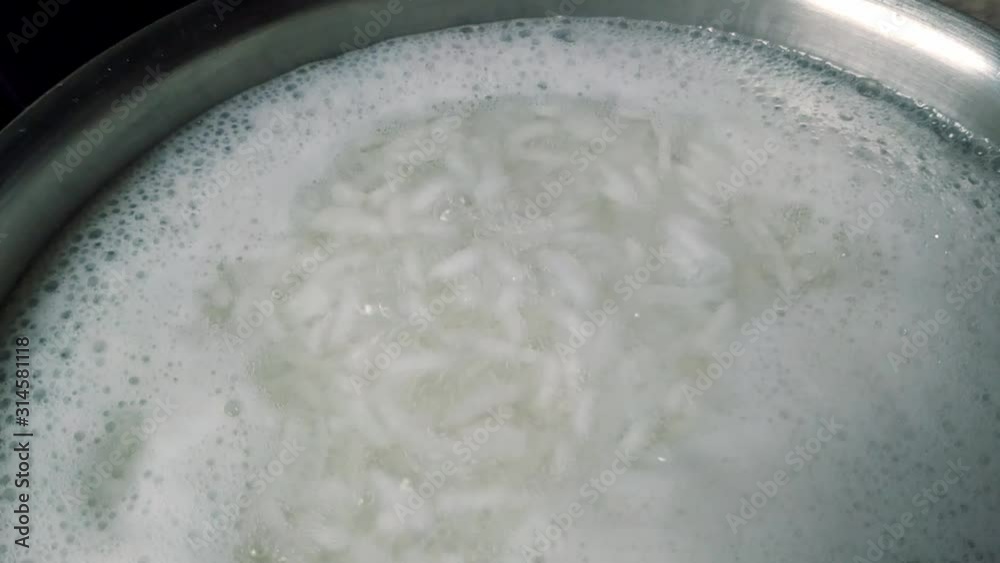 Extreme closeup of boiling rice grains in hot water in a steel vessel