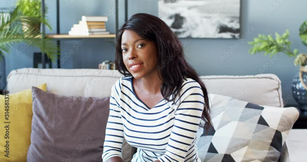 Pretty young African American woman sitting on the sofa in the cozy ...